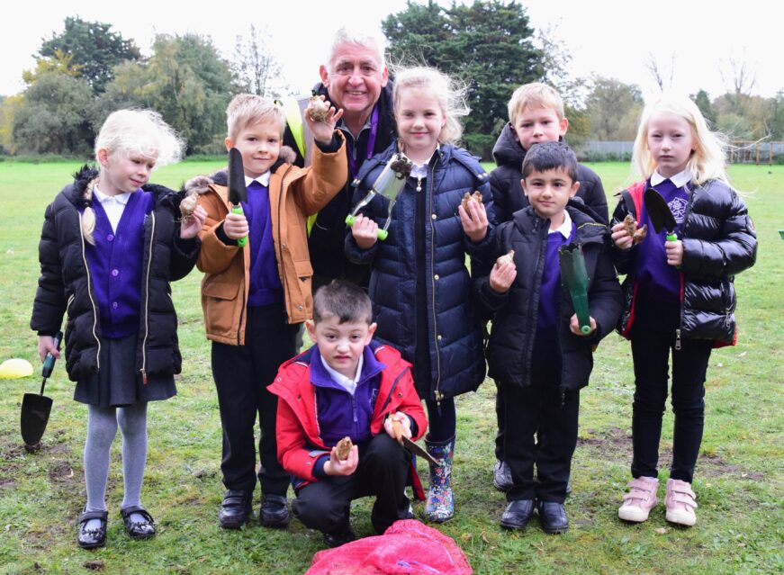 Some KS1 children show Mr Morris how to plant bulbs correctly_